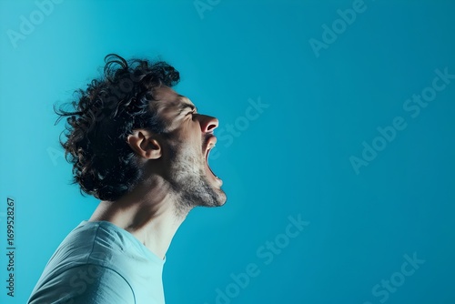 Side view, profile photo of a man shouting with his mouth wide open, isolated on a blue background. Concept with copy space.