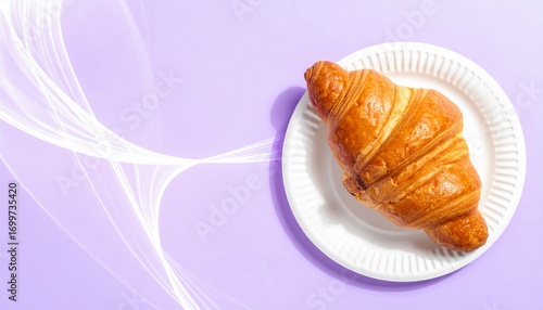 A freshly baked golden brown croissant is served on a simple white paper plate, captured from a top-down perspective against a vibrant purple background with elegant, flowing abstract light waves