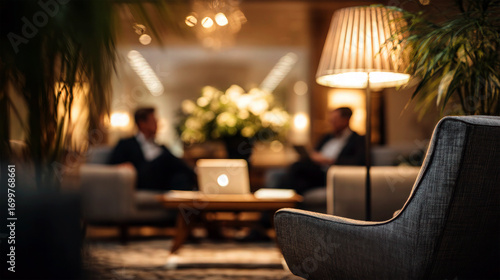 Wallpaper Mural Plush gray armchair in foreground, warm lamp and plants in a hotel lobby where two businessmen talk by a glowing laptop, soft bokeh lights, luxury hospitality atmosphere Torontodigital.ca