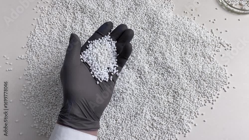 Close-up a scientist in a laboratory in black gloves checks the quality of a batch of white thermoplastic granules. Slow motion.