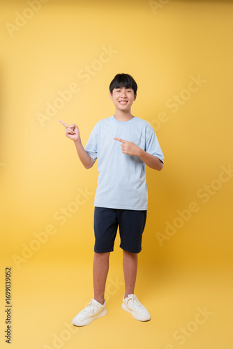 Smiling young person points off camera dressed casually against vibrant yellow backdrop Friendly pose