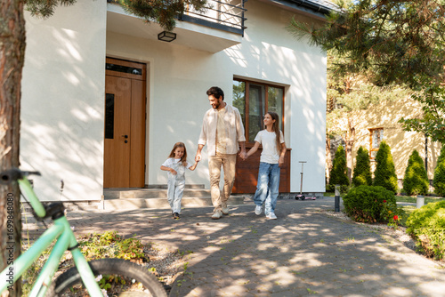 Schilderij op canvas Happy family leaving home holding hands in front of house