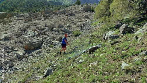 A guy in a cowboy hat climbs a rocky slope on the way to the Alaudin Lakes in Tajikistan. Tourism and freedom. Adventures and travels