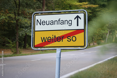 Ein Ortsausgangsschild vor einer Landstraße zeigt in Richtung NEUANFANG und verlässt WEITER SO
