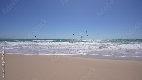 Tarifa, Spain – View of sandy beach with ocean waves and kitesurfers in the sky.