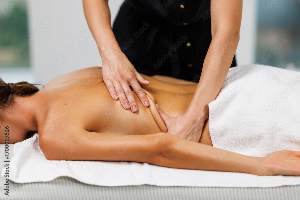 Fototapeta premium Relaxed woman while massage therapist massages her back, applying pressure to release tension in the woman muscles