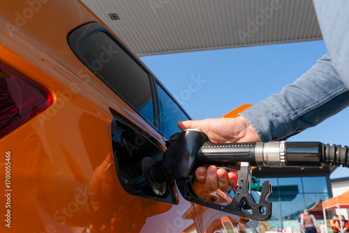 Close-up of a Man refuelling orange car at gas fuel station. Male filling diesel at petrol station using a fuel nozzle
