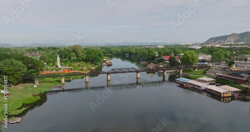 Serene View of Iconic Bridge Over River Kwai in Kanchanaburi Surrounded by Lush Greenery, Calm Waters, and Distant Hills Landscape