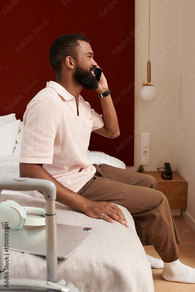 Fototapeta premium Relaxed black man enjoying a call in a modern hotel room while on vacation