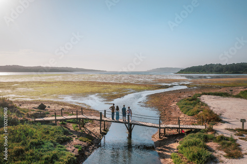 Fotografie Drone view of the wooden bridge crossing the Óbidos Lagoon at sunset, Portugal, surrounded by golden light, calm waters and scenic coastal nature