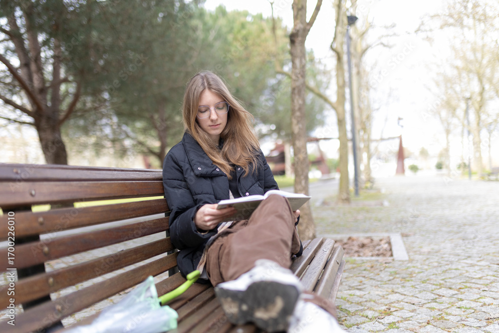 Obraz premium Young woman reading book on park bench