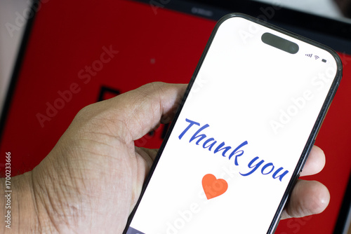 Hand holding mobile phone with the Thank you message along with the heart symbol with the red background. Feb 14, lovers day or valentines day concept
