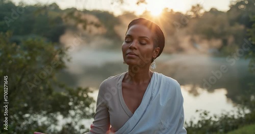 As sunrise brightening lakeside, breathing woman forming mudra on yoga mat at dawn, embracing light