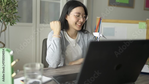 Young Thai woman working on a laptop at home with a wind turbine model beside her.