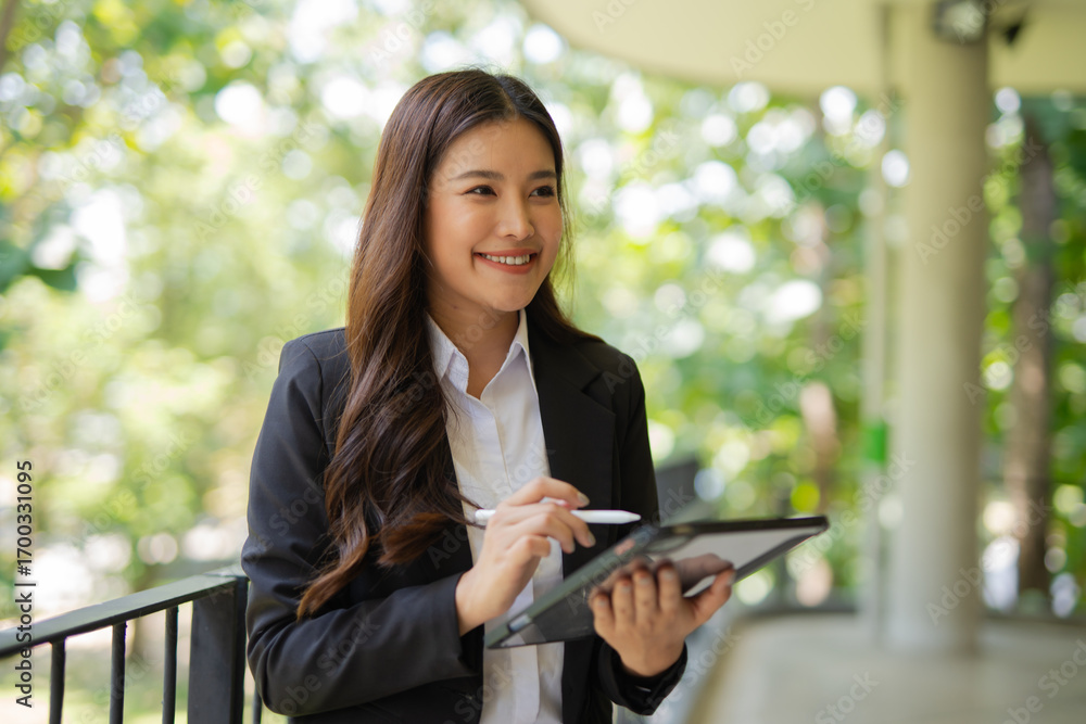 © maeching - Asian businesswoman standing in front of modern business building and using tablet to work. © maeching - Asian businesswoman standing in front of modern business building and using tablet to work.