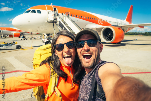 Young happy caucasian couple taking selfie portrait on departure or arrival destination for vacation on sunny autumn day. Budget student travelers, vacationist, explorers having fun. Weekend escape