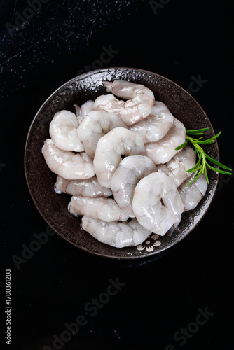 Fresh Raw Peeled Shrimp in Bowl with Green Herbs on Black Background