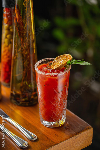 A classic Bloody Mary cocktail served in a crystal glass with salted rim, ice cubes, and garnished with a dried lime slice and fresh parsley, set on a wooden table.