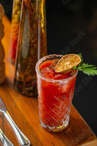 A classic Bloody Mary cocktail served in a crystal glass with salted rim, ice cubes, and garnished with a dried lime slice and fresh parsley, set on a wooden table.