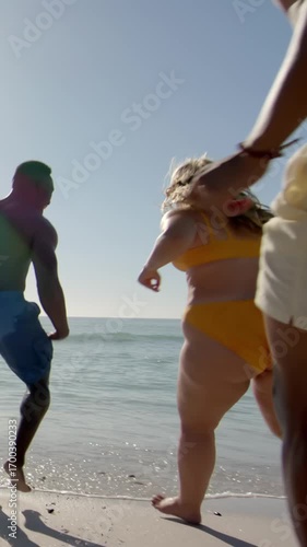 Vertical video: Gentle waves luring diverse friends racing in swimsuits into surf at beach