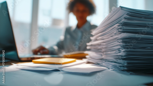 Overwhelmed professional drowning in paperwork, typing intensely with laptop amid mounting deadline stress and workplace pressure