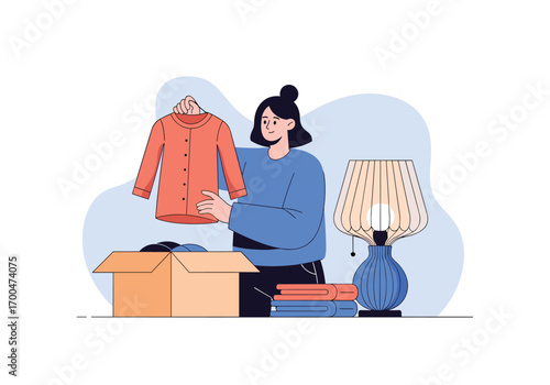 Woman packing clothes and lamp into a cardboard box for moving decluttering or donation