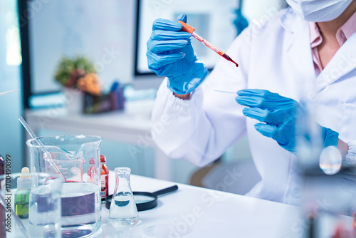 Female scientist in protective mask and gloves analyzing blood samples in test tubes inside a modern laboratory, symbolizing medical diagnostics, healthcare research, and scientific innovation.