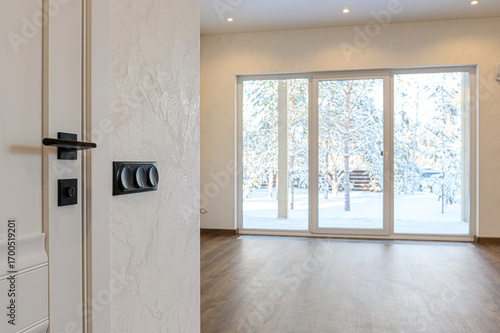 A modern interior featuring a door with black hardware, textured walls, and a large sliding glass door with a snowy outdoor view