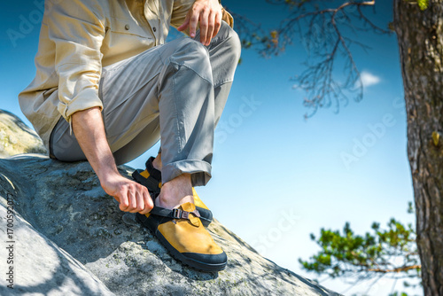 Closeup of man adjusting yellow hiking sandals on rock, trekking footwear for outdoor adventure and travel