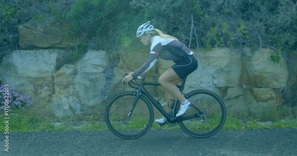 Naklejka premium Pedaling helmeted cyclist wearing cycling attire along paved park path, with black bicycle