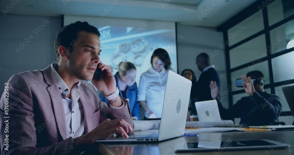Fototapeta premium Man in blazer talking on smartphone while typing on laptop in meeting room, with projection screen
