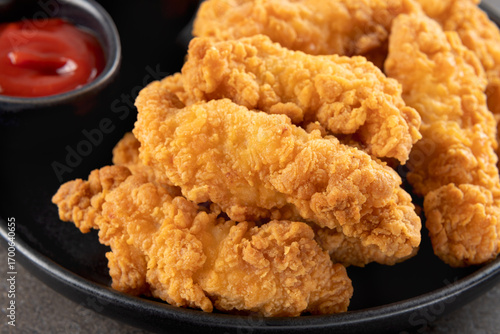 Crispy chicken breast strips with ketchup on a dark background. Close-up. Fast food.