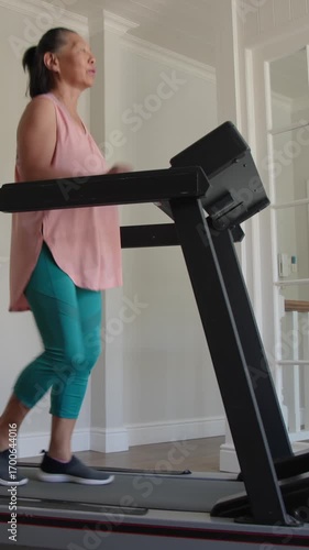 Vertical video: Asian senior woman stepping onto home treadmill jogging until spouse offering towel