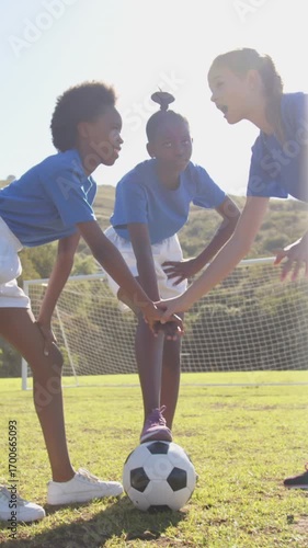 Vertical video: Diverse girls huddling over soccer ball at park on pep call raising, handshaking