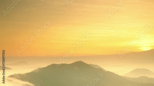 Golden sunrise illuminates misty mountain range with soft light and peaceful atmosphere