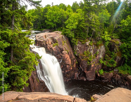 Waterfall cascading over red rock cliffs into a lush forest