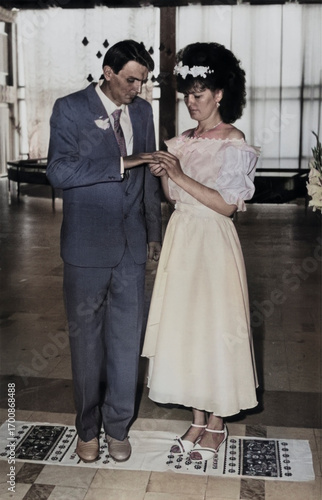 Lozovaya, UkrSSR, USSR - circa 1988: Vintage portrait of a bride and groom. The bride puts a wedding ring on the groom. Retro photo