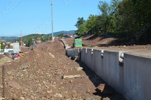 Construction site with ground stabilization works, including retaining wall, piling, soil nails, and steel reinforcements. Heavy machinery in use to secure a landslide area with engineering solutions 