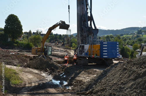 Construction site with ground stabilization works, including retaining wall, piling, soil nails, and steel reinforcements. Heavy machinery in use to secure a landslide area with engineering solutions 