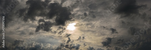 dramatic stormy sky with dark clouds, dense atmospheric haze and bright sunlight shining through. widescreen panoramic photo of natural mystical cloudscape. moody cloud background. aspect ratio 15:5
