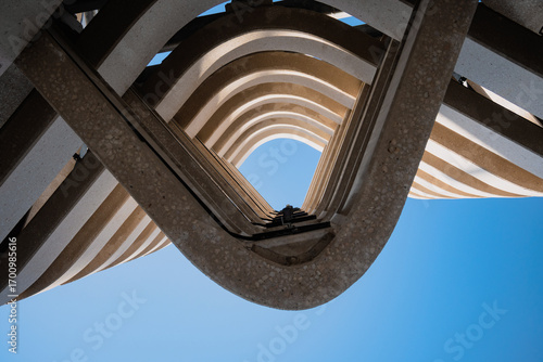 A stunning upward view of a spiraling architectural structure against a vibrant blue sky, highlighting symmetry, geometry, and modern design elements in an artistic composition.