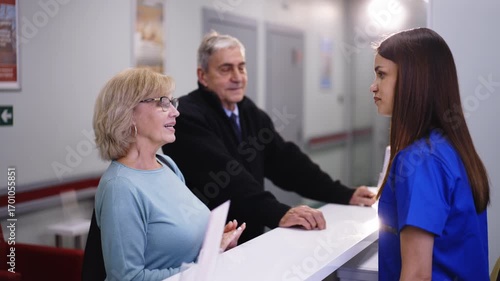 Elderly couple talking with a receptionist at a medical center.
