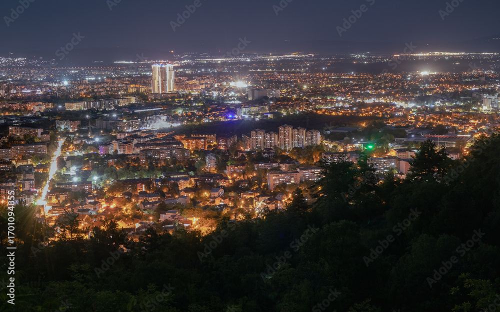 Fototapeta premium night cityscape from a high vantage point, with the glowing lights of a bustling city stretching to the horizon. A prominent skyscraper stands out 