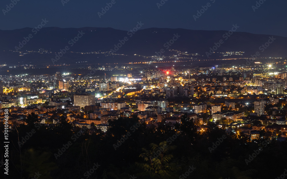 Obraz premium panoramic night view of a sprawling cityscape, with the illuminated buildings and streets of Skopje nestled against the backdrop of mountains
