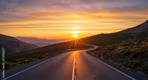 Winding road leads to a vibrant sunrise, casting golden light on the landscape and asphalt