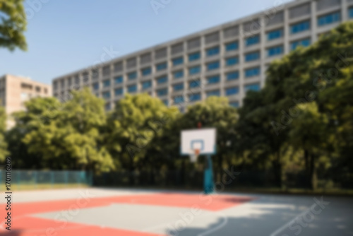 Blurry image of a modern basketball court located in the courtyard of a university building and there are many trees planted around it, blurred background.