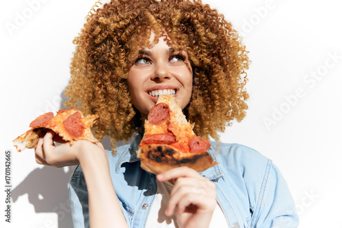 Happy young woman enjoying delicious pizza, showcasing curly hair and vibrant smile, with bright background emphasizing a joyful eating concept