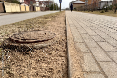 Fotografija A iron manhole above an observation well is located next to a dry grass pedestri