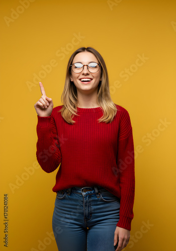 Excited young woman with glasses points upwards, having a brilliant idea or making an announcement.