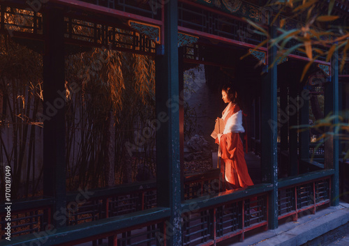 Woman in traditional red hanfu admiring the serene outdoor scenery at sunset.